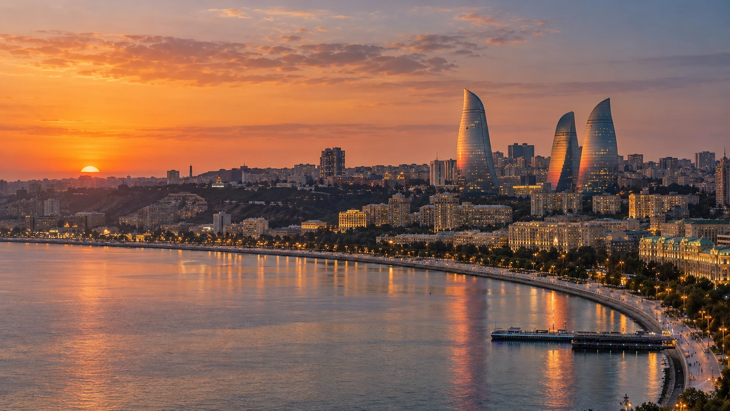 The sun setting behind the Baku skyline with the Flame Towers above the lit seafront